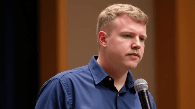 Young man speaking into a microphone during an event or presentation.