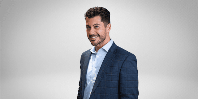 A smiling man in a business suit against a simple background