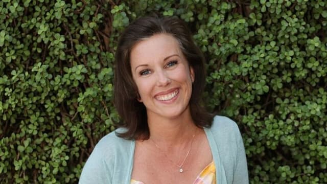 Katrina Foe smiling in front of a green leafy wall outdoors.