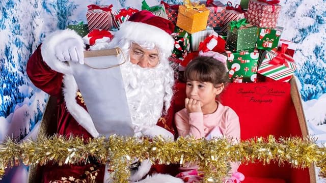 A joyful holiday photo with Santa and a young girl, surrounded by Christmas gifts, capturing a special moment.