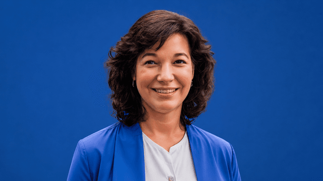 Dr. Leott smiles in a blue blazer against a blue background, representing her women's health education platform.