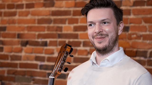 "Troy Serson, guitar instructor, smiling with guitar in hand, offering personalized, online lessons to students of all ages."