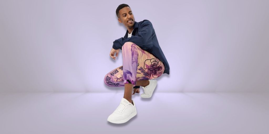 Man crouching in colorful patterned pants and white sneakers against a light purple background.