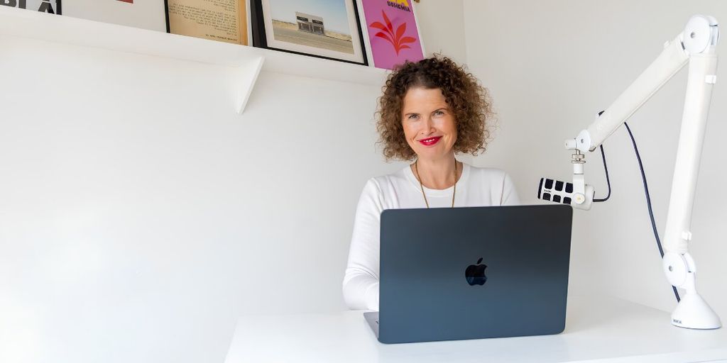 Dr Kate Armstrong seated behind a laptop with a podcast microphone in a bright home office.
