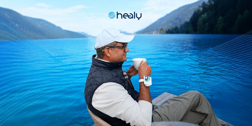 Person wearing a Healy device while enjoying a lakeside view with a cup of coffee.