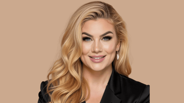 Portrait of a confident blonde woman with soft waves, wearing a black blazer and minimal makeup, smiling against a beige background.