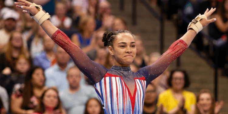 A female gymnast celebrates her routine in a colorful, sparkly leotard.