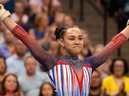 A female gymnast celebrates her routine in a colorful, sparkly leotard.