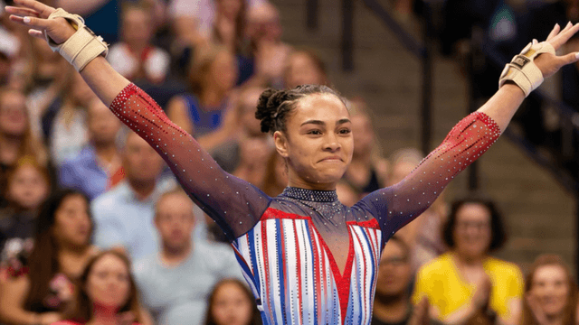 A female gymnast celebrates her routine in a colorful, sparkly leotard.