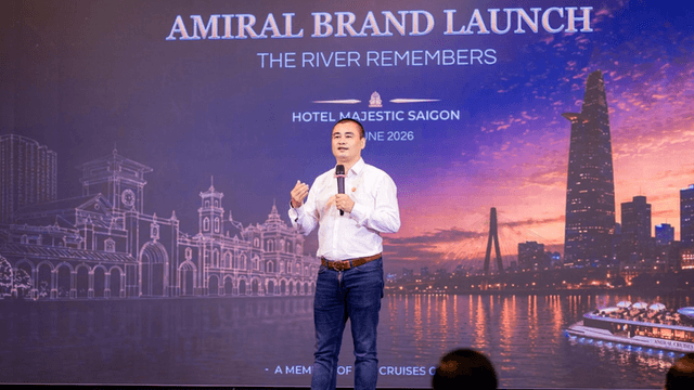 A speaker presenting at the Amiral brand launch event in front of a city skyline backdrop