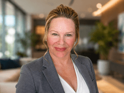 Professional woman in a gray blazer smiling in a modern office setting