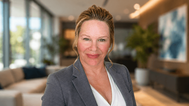 Professional woman in a gray blazer smiling in a modern office setting