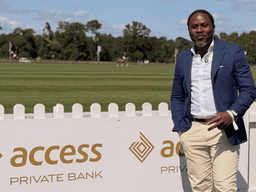 Man in a blue blazer and beige pants poses beside Access Private Bank sign