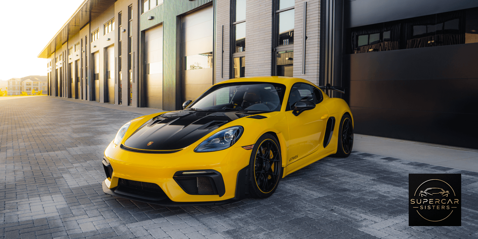 A yellow Porsche 718 GT4 parked in front of a modern garage.