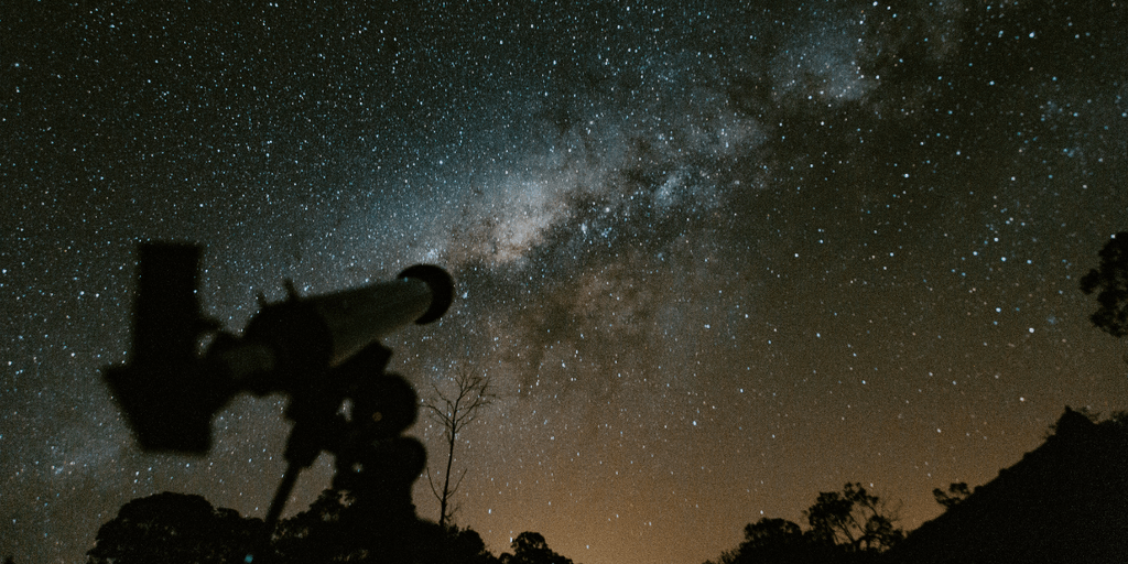 Telescope silhouette against a starry night sky and the Milky Way galaxy