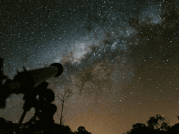 Telescope silhouette against a starry night sky and the Milky Way galaxy