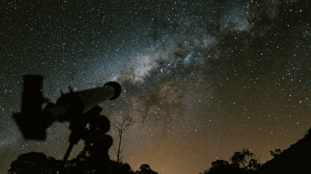 Telescope silhouette against a starry night sky and the Milky Way galaxy