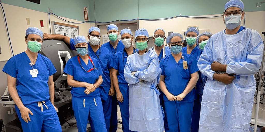 Surgical team in blue scrubs, masks, and gowns posing in an operating room