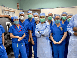 Surgical team in blue scrubs, masks, and gowns posing in an operating room