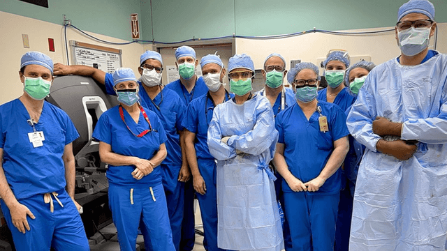 Surgical team in blue scrubs, masks, and gowns posing in an operating room