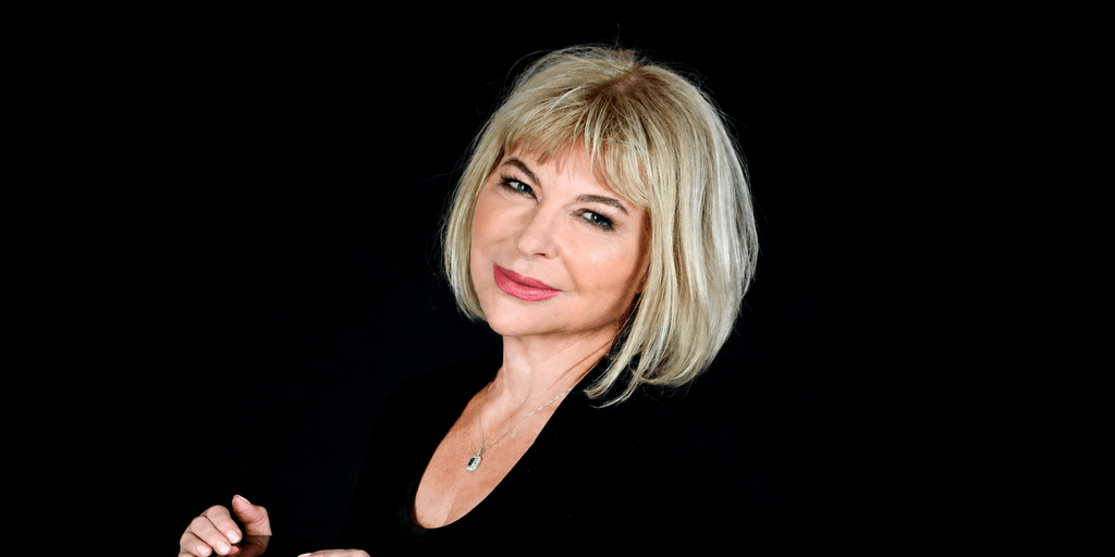A woman with blonde hair smiles confidently against a black background