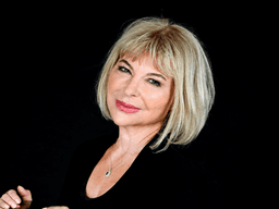A woman with blonde hair smiles confidently against a black background