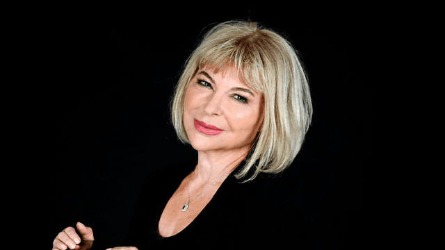 A woman with blonde hair smiles confidently against a black background