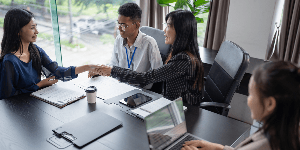 Four professionals in a meeting space engaging in conversation and shaking hands