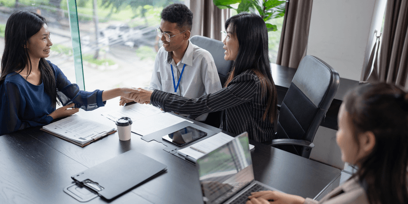 Four professionals in a meeting space engaging in conversation and shaking hands