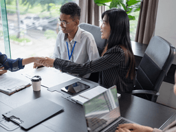 Four professionals in a meeting space engaging in conversation and shaking hands