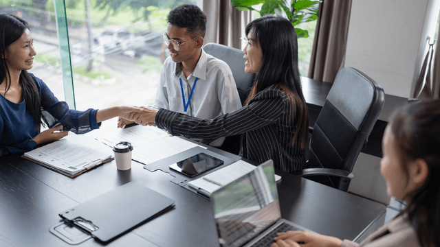 Four professionals in a meeting space engaging in conversation and shaking hands