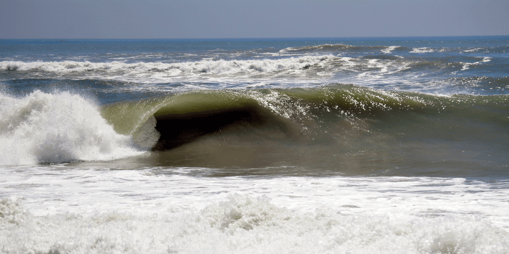 A powerful ocean wave curls dramatically under a bright blue sky