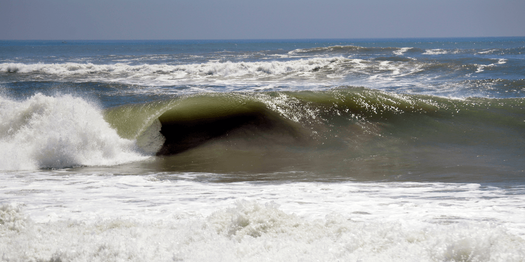 A powerful ocean wave curls dramatically under a bright blue sky