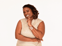 Woman with curly hair in a shimmering dress smiling and posing confidently