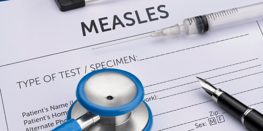 Medical paperwork for measles testing with a stethoscope, syringe, and pen.