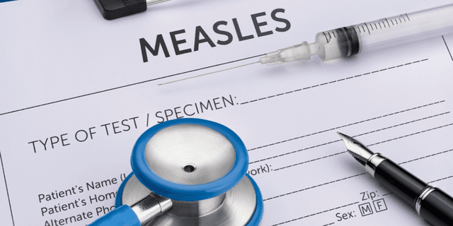 Medical paperwork for measles testing with a stethoscope, syringe, and pen.