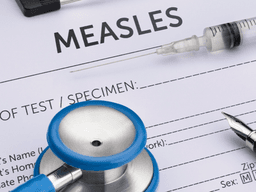 Medical paperwork for measles testing with a stethoscope, syringe, and pen.