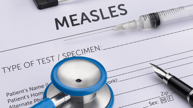 Medical paperwork for measles testing with a stethoscope, syringe, and pen.