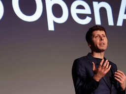 Person speaking on stage with OpenAI logo in the background