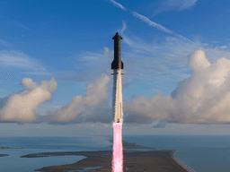 A rocket launches into a clear sky over a coastal landscape with clouds