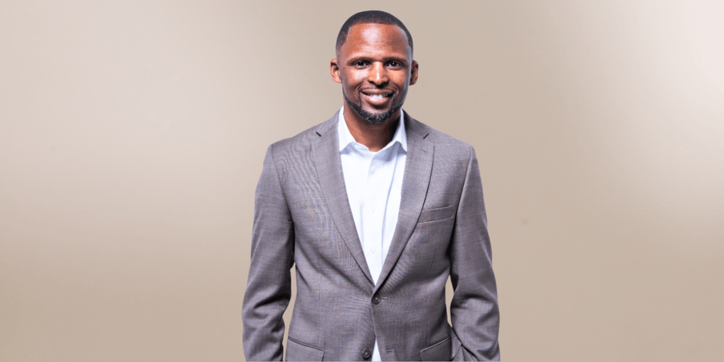 Smiling man in a brown suit and white shirt against a neutral background