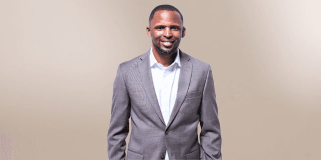 Smiling man in a brown suit and white shirt against a neutral background