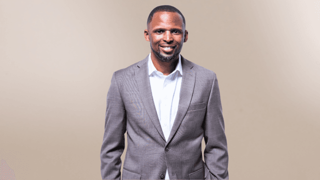 Smiling man in a brown suit and white shirt against a neutral background