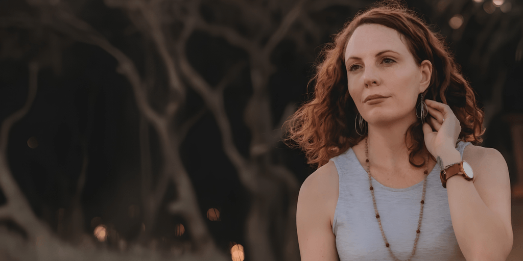 A woman with curly hair wearing a sleeveless top, gazing thoughtfully outdoors
