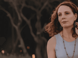 A woman with curly hair wearing a sleeveless top, gazing thoughtfully outdoors