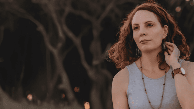 A woman with curly hair wearing a sleeveless top, gazing thoughtfully outdoors