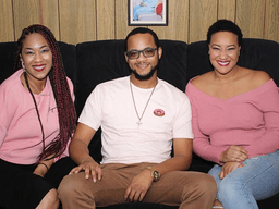 Three people sitting on a couch wearing pink clothing, smiling at the camera.