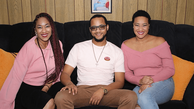 Three people sitting on a couch wearing pink clothing, smiling at the camera.