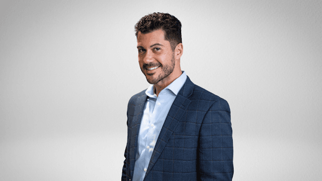 A smiling man in a business suit against a simple background