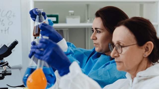 Two scientists in lab coats conduct experiments with colorful liquid in flasks